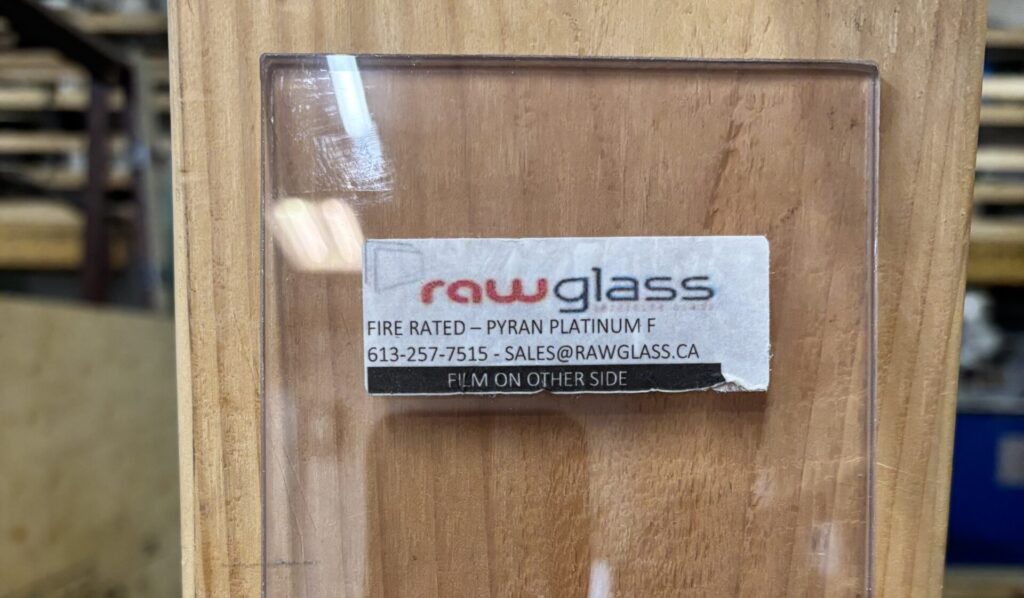 Fire-rated Pyran Platinum F glass sample with Raw Glass sticker showing phone and email contacts